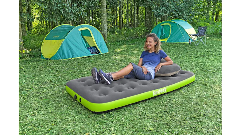 A camper is relaxing on an inflatable mattress with a pillow in a wooded campground setting A camper is relaxing on an inflatable mattress with a pillow in a wooded campground setting