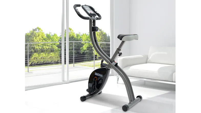 A stationary folding exercise bike positioned inside a brightly lit, modern living room space A stationary folding exercise bike positioned inside a brightly lit, modern living room space