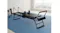 A black Pilates reformer positioned on a blue rug inside a bright room with weights visible A black Pilates reformer positioned on a blue rug inside a bright room with weights visible