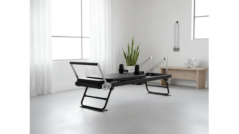 A Pilates reformer in a minimalist room featuring white curtains, a potted plant, and a wooden bench A Pilates reformer in a minimalist room featuring white curtains, a potted plant, and a wooden bench
