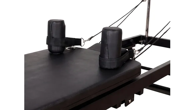 A close-up detail of two cylindrical padded shoulder rests and connected straps on a black Pilates reformer carriage A close-up detail of two cylindrical padded shoulder rests and connected straps on a black Pilates reformer carriage