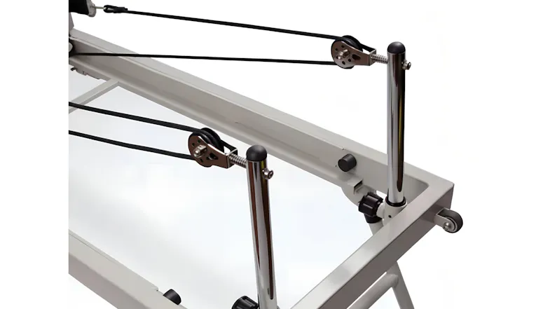 A close-up detail view of the Pilates reformer's chrome rear upright bars, black ropes, and pulley wheel system A close-up detail view of the Pilates reformer's chrome rear upright bars, black ropes, and pulley wheel system