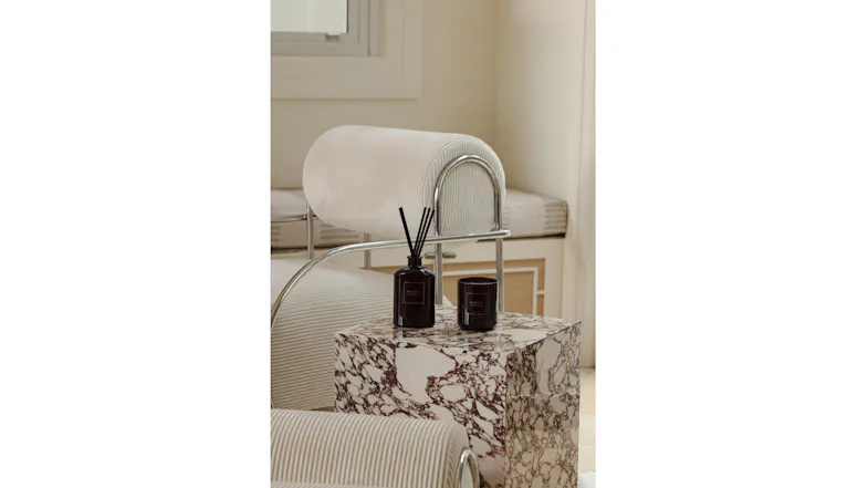 Moss St. reed diffuser and matching candle set on a marble block table beside a contemporary chair Moss St. reed diffuser and matching candle set on a marble block table beside a contemporary chair