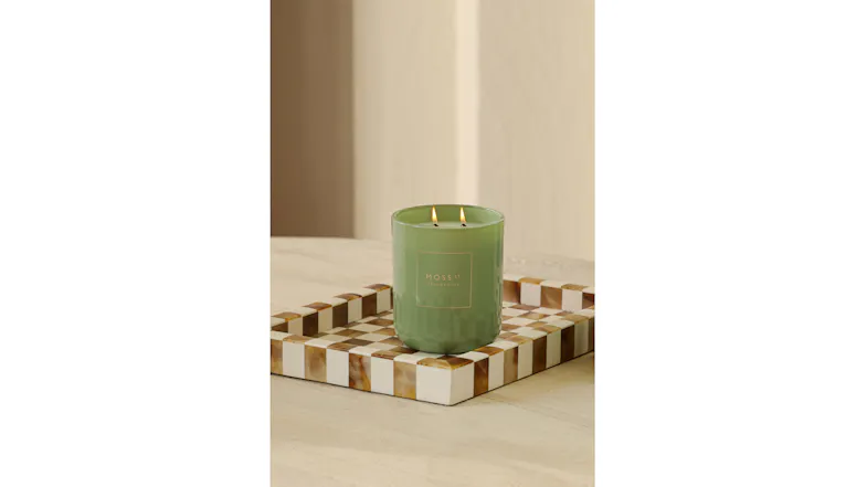 Close-up view showing a lit green candle on a brown checkered tray Close-up view showing a lit green candle on a brown checkered tray