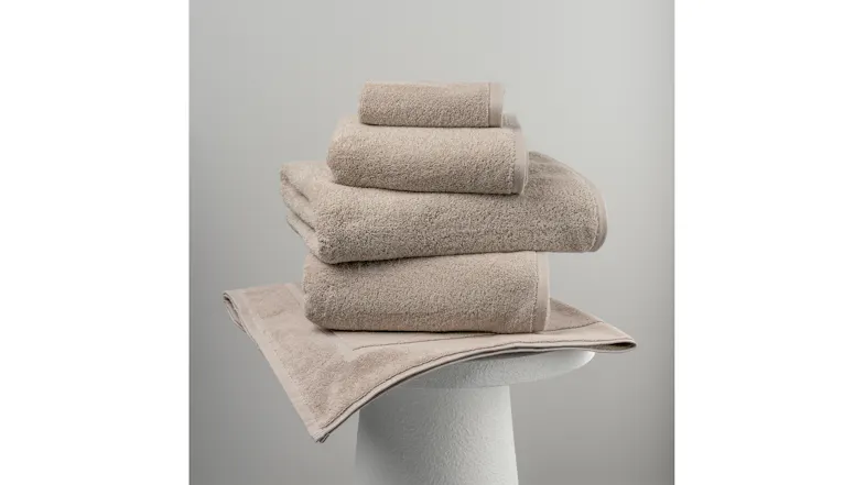A stack of natural towels displayed on a matching bath mat atop a white pedestal A stack of natural towels displayed on a matching bath mat atop a white pedestal