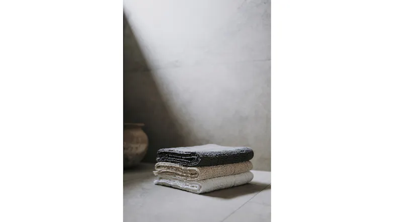 A stack of folded towels in linen, beige, and charcoal grey rests on a bathroom countertop in soft natural light A stack of folded towels in linen, beige, and charcoal grey rests on a bathroom countertop in soft natural light
