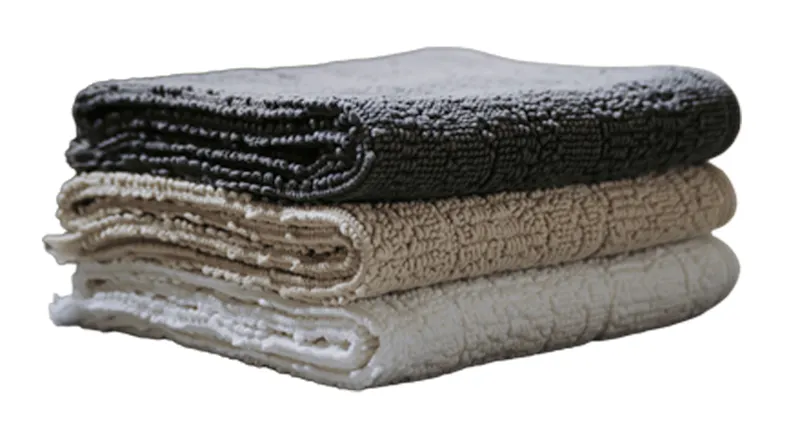 Stack of three folded textured Baksana Lisbon bath mats in Slate, Linen, and White Stack of three folded textured Baksana Lisbon bath mats in Slate, Linen, and White