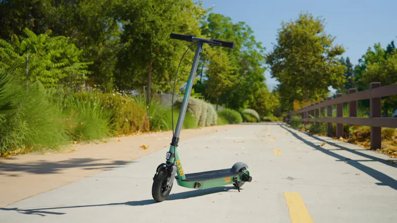 Outdoor view of a mint green electric scooter on a recreational trail lined with lush vegetation Outdoor view of a mint green electric scooter on a recreational trail lined with lush vegetation