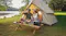 Anker SOLIX portable power station charging devices at a lakeside campsite beside a tent and picnic table Anker SOLIX portable power station charging devices at a lakeside campsite beside a tent and picnic table