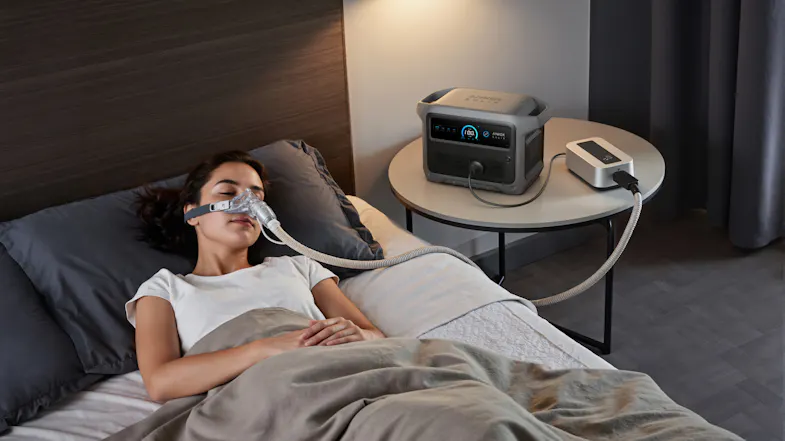 Anker SOLIX portable power station powering a bedside CPAP machine while a person rests in bed Anker SOLIX portable power station powering a bedside CPAP machine while a person rests in bed