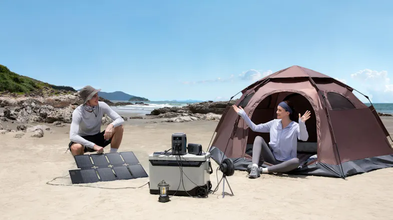 Beach campsite featuring a portable power station, foldable solar panels, and a cooling fan Beach campsite featuring a portable power station, foldable solar panels, and a cooling fan