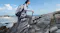 A hiker traversing a rocky coastline with a portable power station for off-grid charging A hiker traversing a rocky coastline with a portable power station for off-grid charging