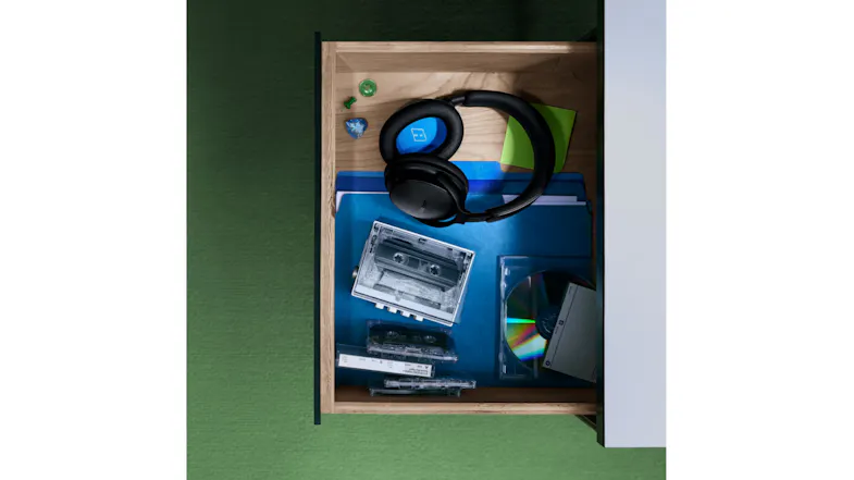 An open wooden desk drawer featuring headphones resting on items An open wooden desk drawer featuring headphones resting on items