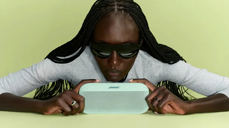 Woman holding the Bose speaker showcasing its compact size Woman holding the Bose speaker showcasing its compact size
