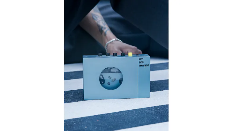 Hand operating the blue cassette player on a striped surface, demonstrating the device's controls Hand operating the blue cassette player on a striped surface, demonstrating the device's controls