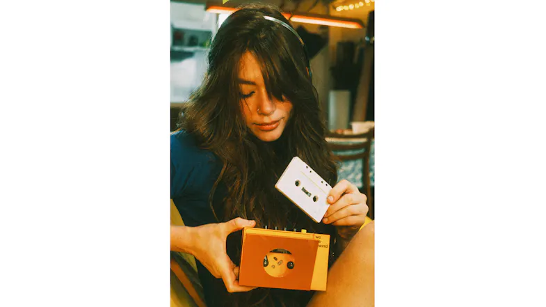 Person holding and using the orange We Are Rewind cassette player while inserting or removing a cassette tape Person holding and using the orange We Are Rewind cassette player while inserting or removing a cassette tape