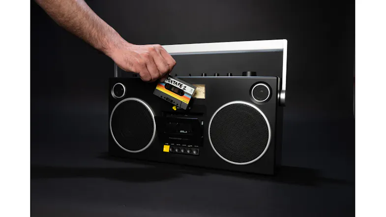 Hand inserting or removing a cassette tape from the boombox, illustrating playback and recording functionality Hand inserting or removing a cassette tape from the boombox, illustrating playback and recording functionality