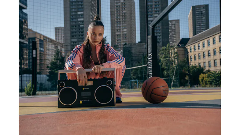 Blaster Curtis cassette boombox placed on an outdoor court next to a basketball, showcasing retro style Blaster Curtis cassette boombox placed on an outdoor court next to a basketball, showcasing retro style