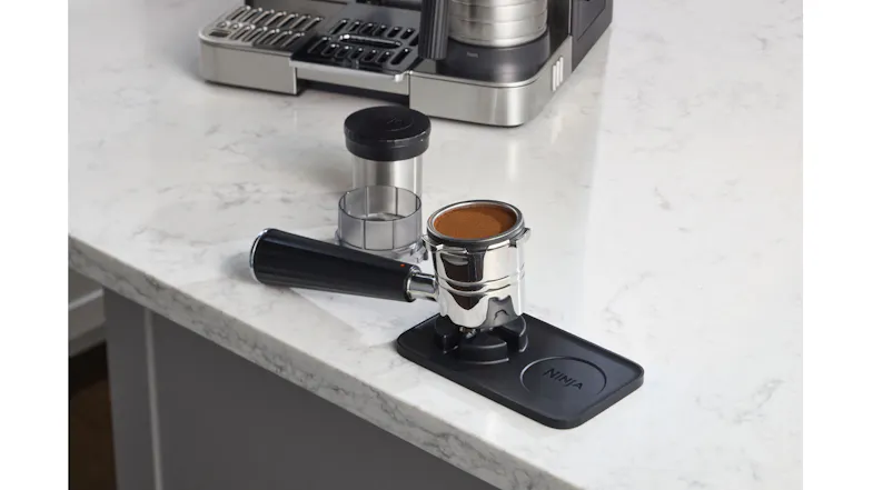 Espresso portafilter filled with coffee grounds resting on a black Ninja tamping mat Espresso portafilter filled with coffee grounds resting on a black Ninja tamping mat