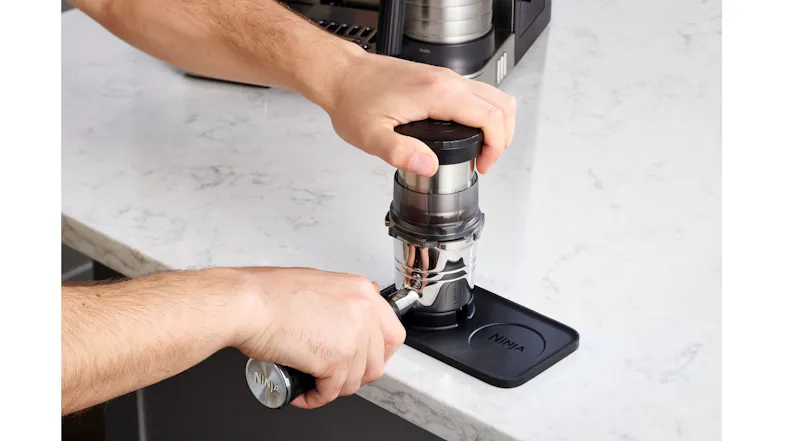 User tamping coffee grounds through a funnel using a Ninja espresso tamper and mat User tamping coffee grounds through a funnel using a Ninja espresso tamper and mat