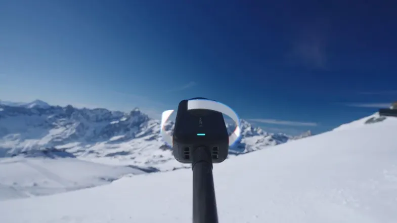 A close-up view of a 360-action camera mounted on a pole, overlooking a snowy mountain landscape A close-up view of a 360-action camera mounted on a pole, overlooking a snowy mountain landscape