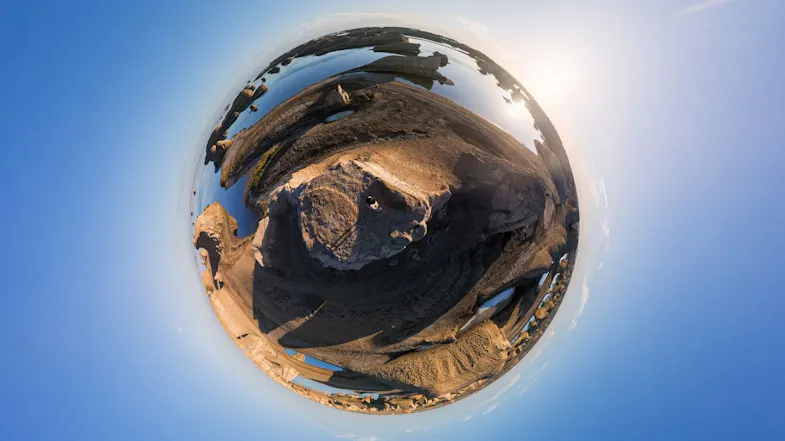 Tiny planet 360 projection of a person standing atop a desert rock formation surrounded by calm water Tiny planet 360 projection of a person standing atop a desert rock formation surrounded by calm water
