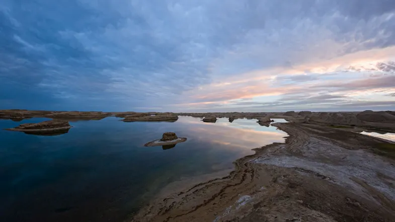 A panoramic view of a desert lake landscape reflecting a soft pink and blue sunset sky A panoramic view of a desert lake landscape reflecting a soft pink and blue sunset sky