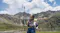 Hiker standing in a grassy mountain valley holding an extended selfie stick with a 360-action camera Hiker standing in a grassy mountain valley holding an extended selfie stick with a 360-action camera