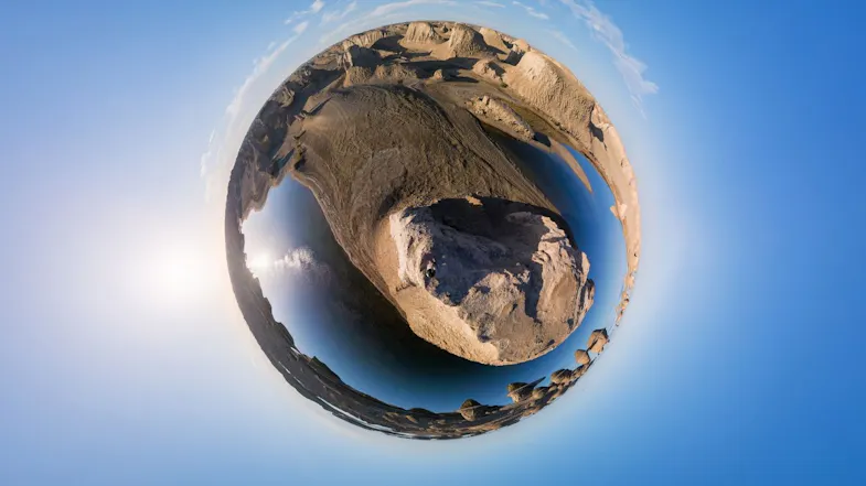 A 360-degree tiny planet aerial view showing a rocky desert landscape and body of water under a clear sky A 360-degree tiny planet aerial view showing a rocky desert landscape and body of water under a clear sky