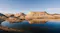 Desert rock formations and sand mounds reflecting a still body of water under a clear blue sky Desert rock formations and sand mounds reflecting a still body of water under a clear blue sky