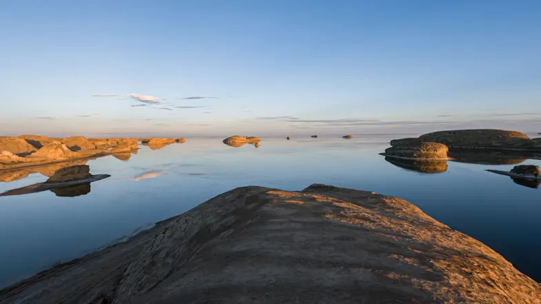 A wide view of calm, reflective water interspersed with desert rock islands during twilight A wide view of calm, reflective water interspersed with desert rock islands during twilight