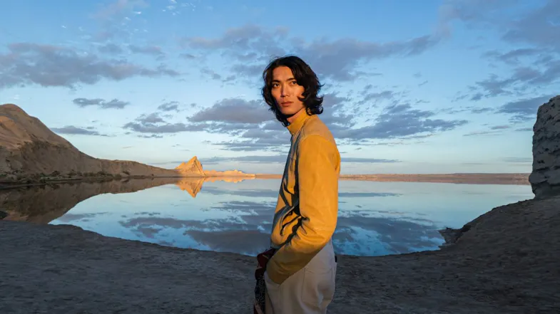 Young man in a yellow jacket standing outdoors beside a reflective desert lake during golden hour Young man in a yellow jacket standing outdoors beside a reflective desert lake during golden hour