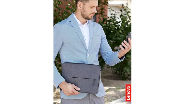 A man in a light blue blazer holds a charcoal grey Lenovo laptop sleeve while looking at his smartphone A man in a light blue blazer holds a charcoal grey Lenovo laptop sleeve while looking at his smartphone