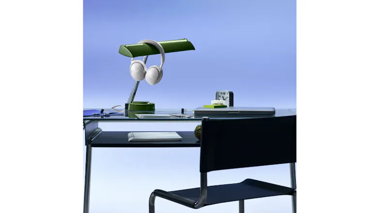 White headphones hanging on a desk lamp showcasing workspace setup White headphones hanging on a desk lamp showcasing workspace setup