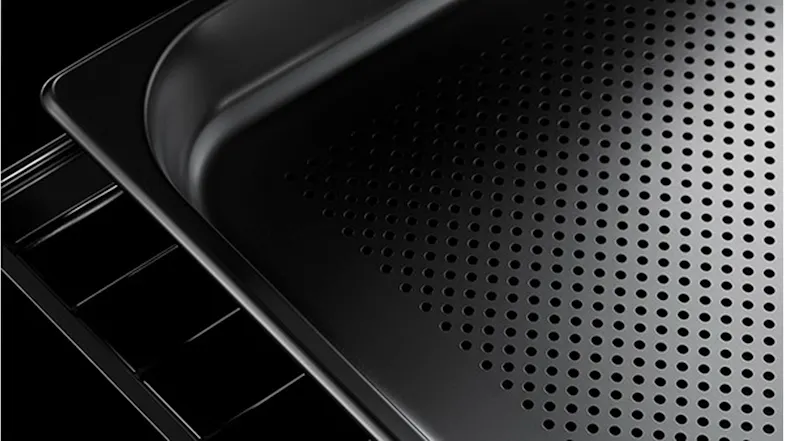 Close-up of a black perforated steam oven tray resting on a wire rack against a dark background Close-up of a black perforated steam oven tray resting on a wire rack against a dark background