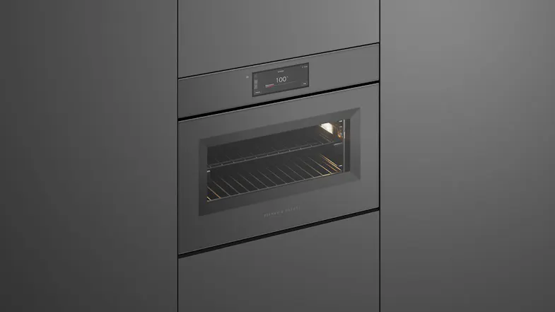 An angled view of a sleek, built-in matte grey Fisher & Paykel oven with an illuminated interior and digital display An angled view of a sleek, built-in matte grey Fisher & Paykel oven with an illuminated interior and digital display