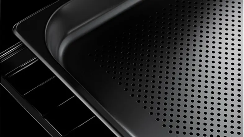 Close-up of a black perforated steam oven tray resting on a wire rack against a dark background Close-up of a black perforated steam oven tray resting on a wire rack against a dark background