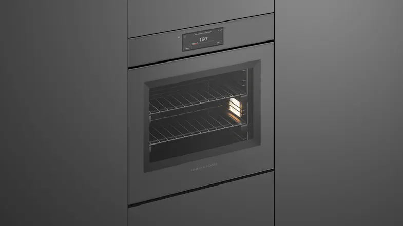 Angled view of a sleek grey built-in oven with an illuminated interior and digital display Angled view of a sleek grey built-in oven with an illuminated interior and digital display
