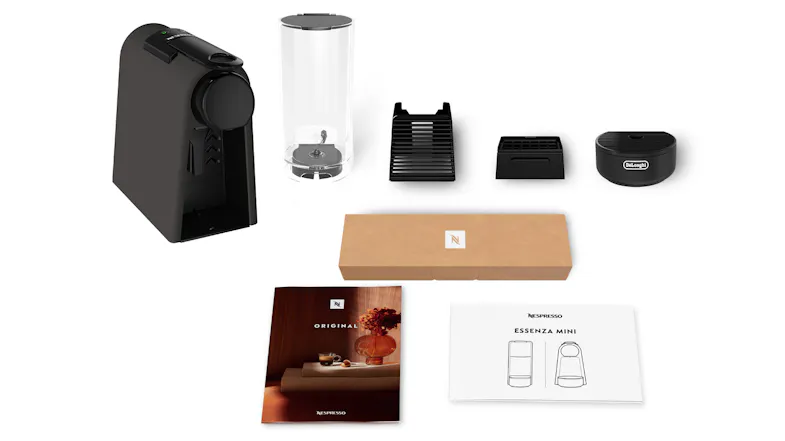 DeLonghi Nespresso Essenza Mini shown unboxed with removable parts, coffee capsules, and manuals DeLonghi Nespresso Essenza Mini shown unboxed with removable parts, coffee capsules, and manuals