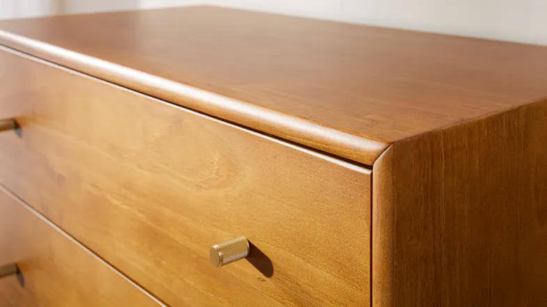 Close-up of wooden dresser corner with warm finish, rounded edges and brass-look handle detail Close-up of wooden dresser corner with warm finish, rounded edges and brass-look handle detail