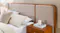 Close-up of wooden bed with beige extended upholstered panel headboard, integrated bedside table and neutral bedding Close-up of wooden bed with beige extended upholstered panel headboard, integrated bedside table and neutral bedding