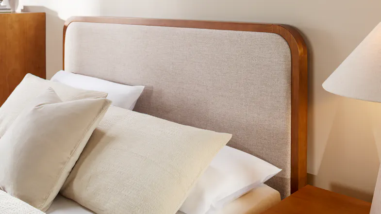 Beige upholstered headboard with rounded wooden frame, styled with neutral pillows and bedside table Beige upholstered headboard with rounded wooden frame, styled with neutral pillows and bedside table