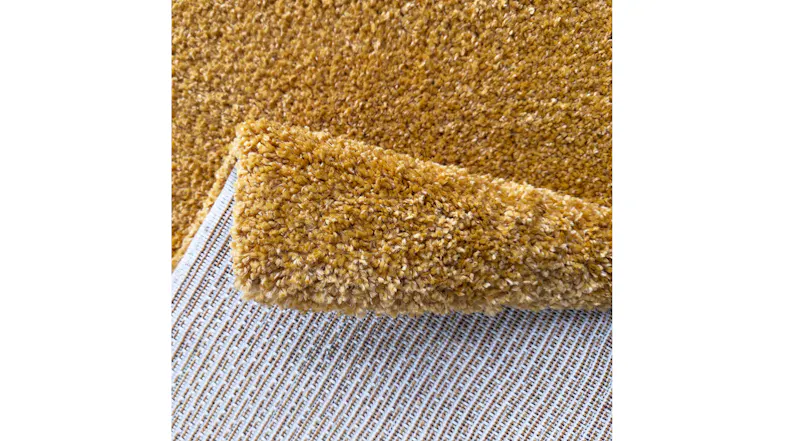 Angled close-up of the rug edge and surface, emphasising the plush texture, dense fibres and warm amber colour Angled close-up of the rug edge and surface, emphasising the plush texture, dense fibres and warm amber colour