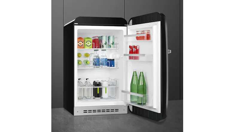 Angled view of a black SMEG compact refrigerator with the door open, displaying drinks and bottle racks inside Angled view of a black SMEG compact refrigerator with the door open, displaying drinks and bottle racks inside