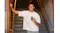 Smiling man standing in a doorway on a staircase, holding a compact Shark cooling device while wearing a white T-shirt Smiling man standing in a doorway on a staircase, holding a compact Shark cooling device while wearing a white T-shirt