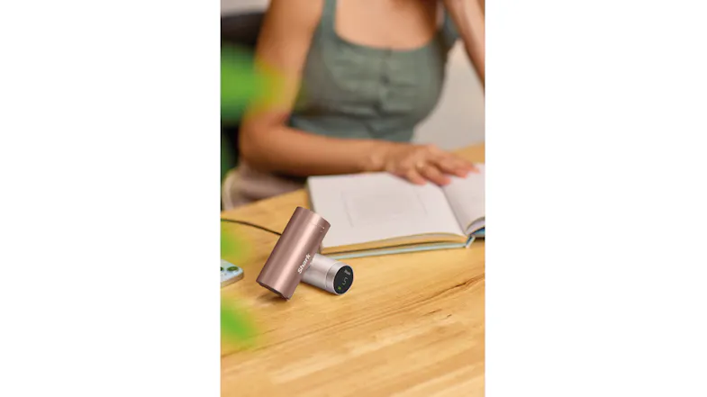 Rose gold Shark ChillPill device resting on a wooden desk next to an open book, with a blurred person in the background Rose gold Shark ChillPill device resting on a wooden desk next to an open book, with a blurred person in the background