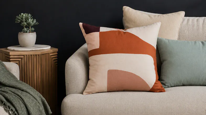 Malaga Terracotta cushion displayed on a beige sofa next to a potted plant and side table Malaga Terracotta cushion displayed on a beige sofa next to a potted plant and side table