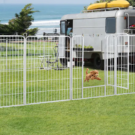 White metal pet fence enclosing a grass yard by an RV camper, with a fluffy brown puppy jumping through the open door panel White metal pet fence enclosing a grass yard by an RV camper, with a fluffy brown puppy jumping through the open door panel