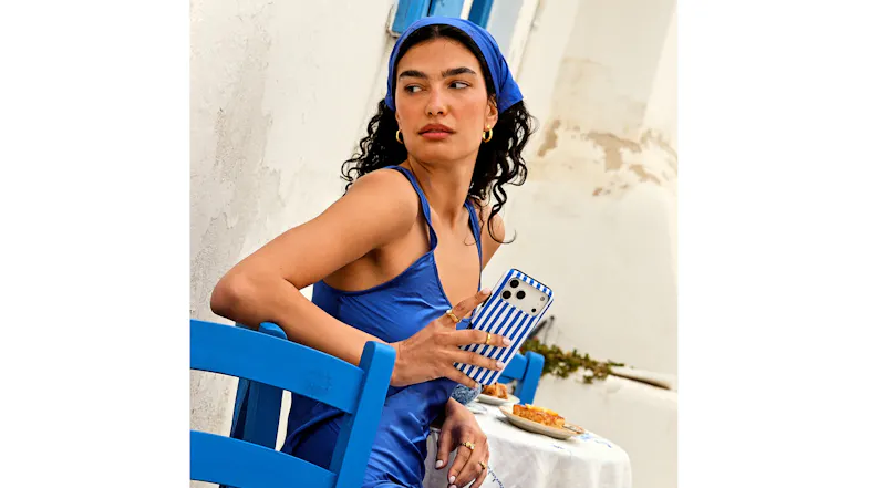 A lady holding a BURGA phone case held beside a café table in a Mediterranean-inspired setting A lady holding a BURGA phone case held beside a café table in a Mediterranean-inspired setting