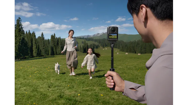 DJI Osmo 360 camera mounted on an extension pole filming people in a grassy park DJI Osmo 360 camera mounted on an extension pole filming people in a grassy park